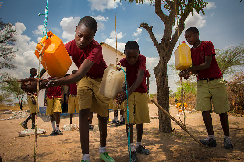 I landsbyen Ikonda vasker Muhoja Mabula, Ngwandu Kashinde og Juma Gisusu seg ved skolens toalett, som Kirkens Nødhjelp har støttet. Foto: Håvard Bjelland / Kirkens Nødhjelp.