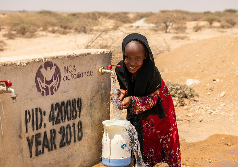 Maryam Abdirzale henter vann fra en brønn Kirkens Nødhjelp har reparert.