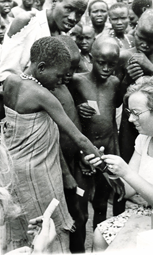 Sykepleier Aud vaksinerer en jente i Sør Sudan. Mange andre mennesker står rundt og venter på sin tur.  