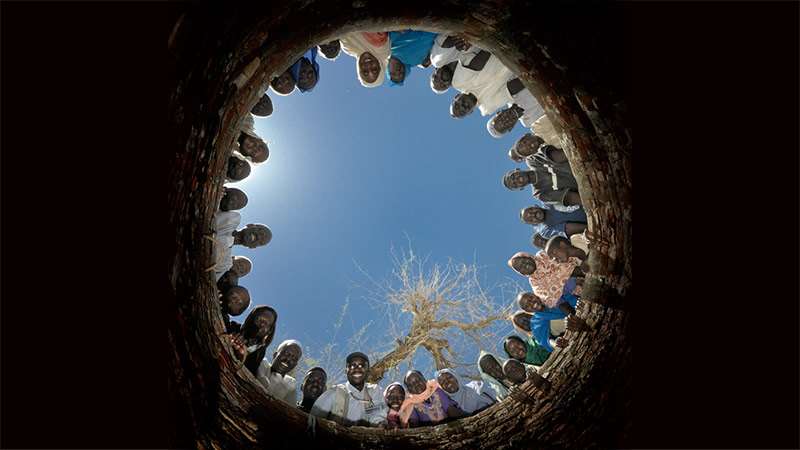 Mennesker i Darfur som ser ned i brønnen de selv har bygd. Foto: Paul Jeffrey / ACT Alliance.
