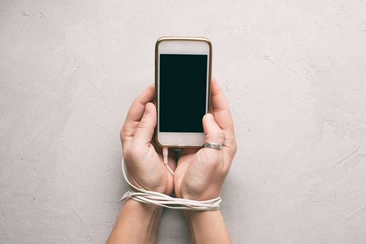 bilde av en mobil som er låst i hendene på et menneske ved hjelp av ledning