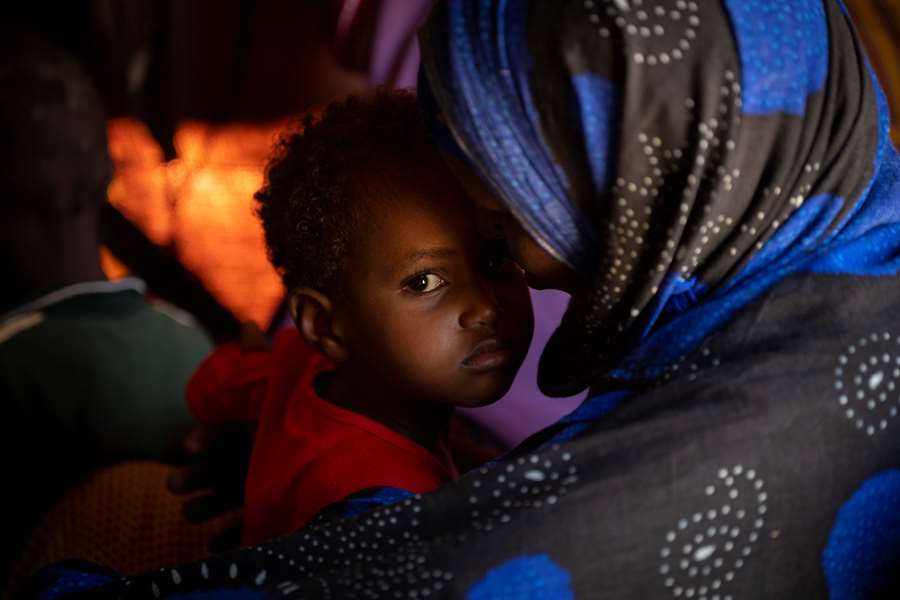 Liten jente som sitter på fanget til moren sin i en leir i Somalia
