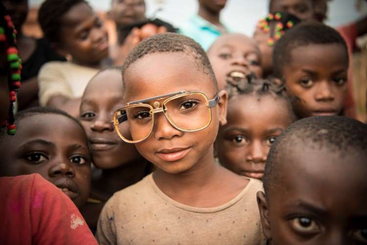 En ung gutt med briller og mange andre barn i bakgrunnen i Angola