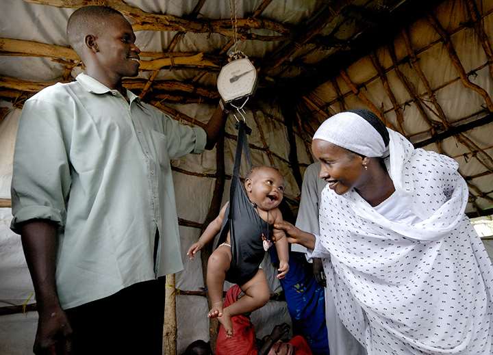 et barn som måler vekten sin mens moren står og smiler og legen er fornøyd også
