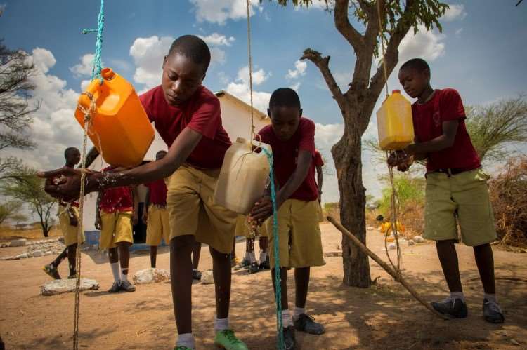 Barn som holder på å få tak i vann i deres store vannflasker